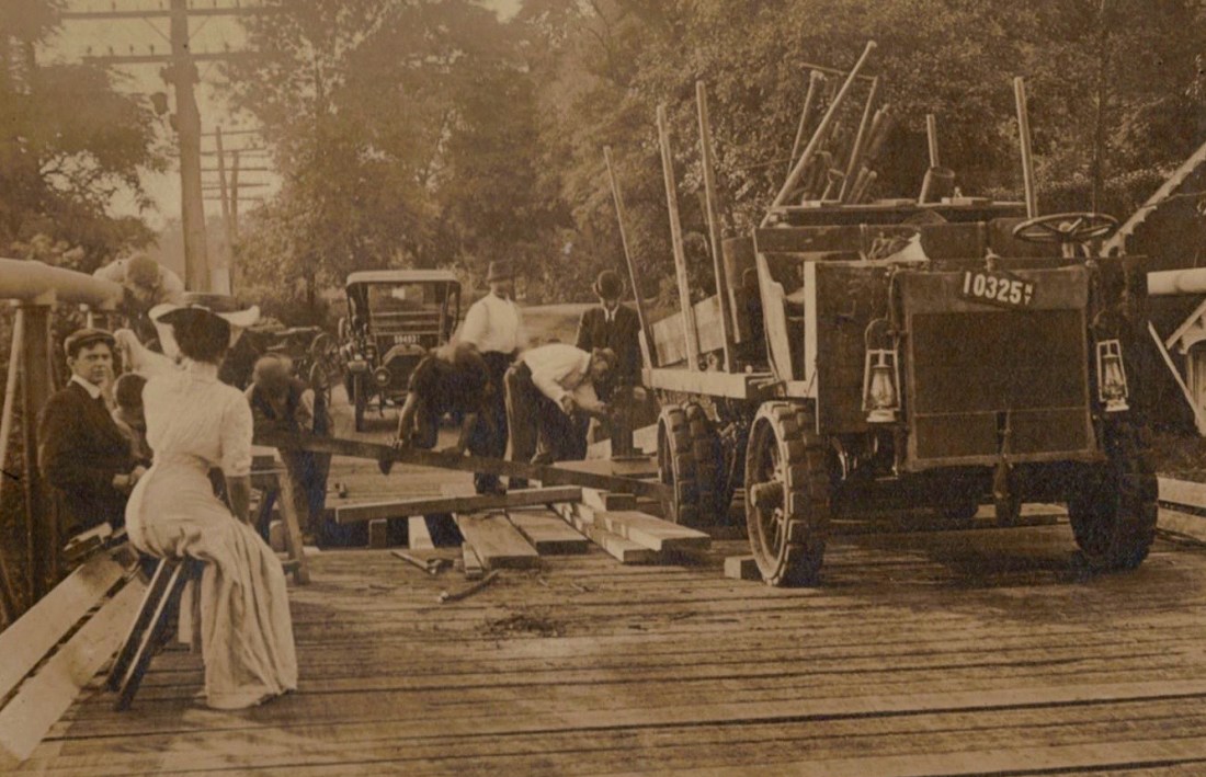 Detail showing David Miller and Aimee Marie Dyckman on the left and the repair crew using a fulcrum in an attempt to raise the rear tire of the 2- to 3-ton vehicle.
